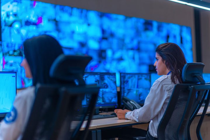 Group of Security data center operators (administrators) working in a group at a CCTV monitoring room while looking at multiple monitors ( computer screens)